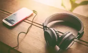 Słuchawki i smartfon leżące na drewnianym stole.