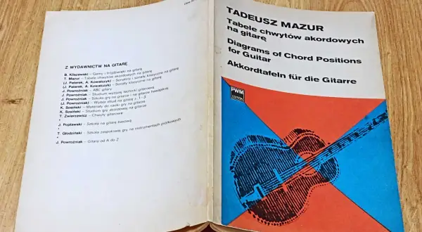Otwarta książka z tabelami chwytów gitarowych i schematycznym rysunkiem gitary.